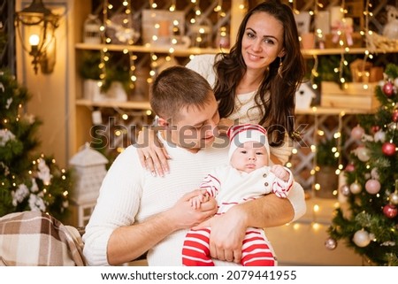 Parents celebrate new year's eve at home with small child, sitting by christmas tree and holding the baby in their arms in anticipation of the coming new year. Young caucasian family