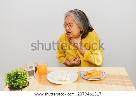 Senior asian woman with acid reflux problem, sore throat. While eating patty, food stuck in the throat, burning sensation in the esophagus, irritation, coughing, suffocation and difficulty swallowing. Royalty-Free Stock Photo #2079461317