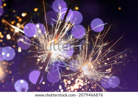 two classic sparklers with purple blurred bokeh lights on a black purple gradient background - new year celebration party banner