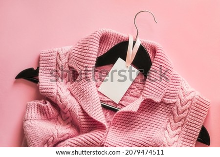 Clothes tag, blank label mockup template to place your design.Knitted pink vest on a black wooden hanger on a pink background. Advertising banner for a clothing boutique.