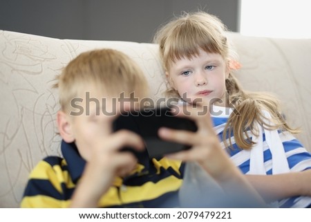 Brother and sister at home on sofa watching on smartphone screen