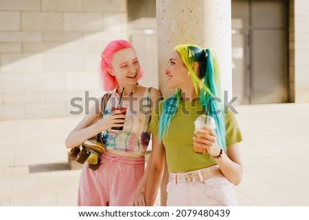 Young lesbian couple smiling and holding hands while drinking beverages outdoors