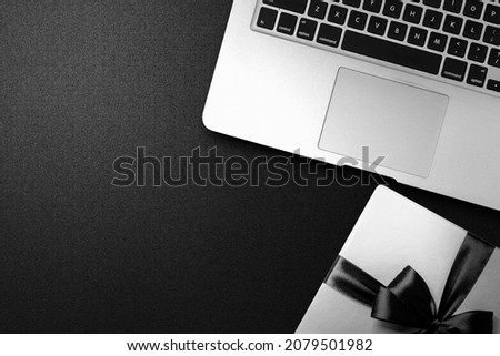 White gift box with a black ribbon and laptop with a black background. Black Friday concept