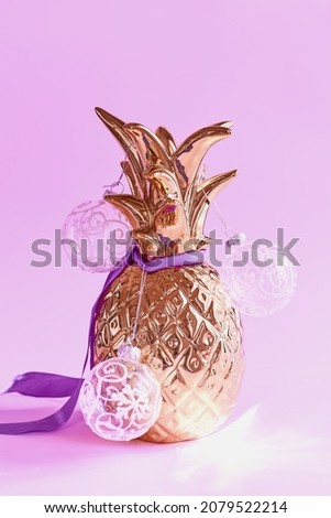 Alternative Christmas tree. Golden pineapple decorated with purple ribbon and transparent Christmas balls on purple background
