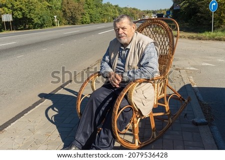 Caucasian senior man resting while sitting in a wicker rocking-chair at roadside at sunny autumnal day