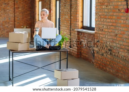 New business premises concept. Online education for women anywhere. Happy caucasian middle age blond lady in headset studying with laptop at new office space taking notes while watching webinar