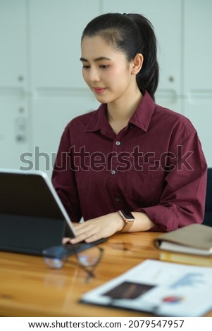 Beautiful young female assistant working on her portable tablet computer in modern office workplace. 
