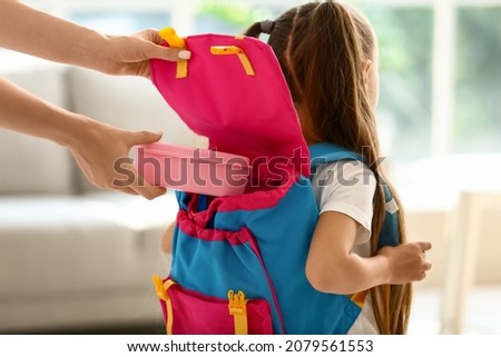 Mother putting school lunch in backpack of her little daughter at home Royalty-Free Stock Photo #2079561553