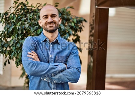 Young hispanic man smiling happy with arms crossed gesture at the city.