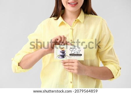 Young woman with gift certificate for massage on light background