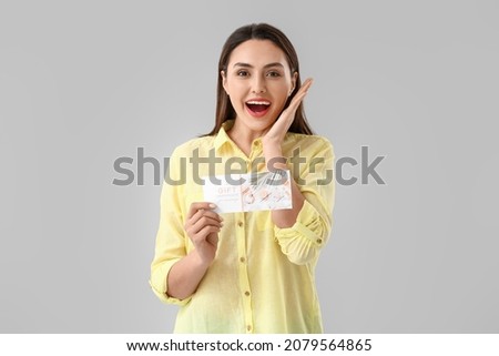 Surprised young woman with gift certificate for massage on light background