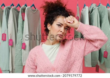 Young sick ill exhausted tired female costumer woman 20s wear sweater stand near clothes rack with tag sale in store showroom put hand on forehead isolated on plain pink background studio portrait.