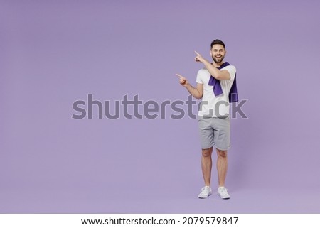 Full size body length happy smiling vivid young brunet man 20s wear white t-shirt purple shirt pointing aside on workspace area copy space mock up isolated on pastel violet background studio portrait.