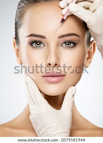 Portrait of young Caucasian woman getting botox cosmetic injection in forehead. Beautiful woman gets botox injection in her face. Royalty-Free Stock Photo #2079581944