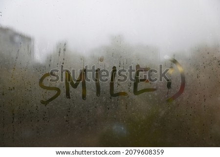 Word SMILE written on foggy window. Rainy weather