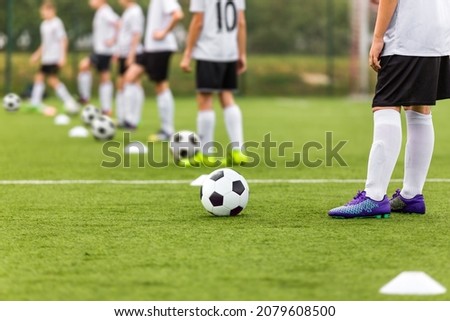 Soccer Players Standing in Line With Soccer Balls on Traininf Unit. Football School For Kids. Young Boys Practicing Soccer on Grass Pitch. Children in White and Black Soccer Kit