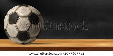 Closeup of an old leather soccer ball on a wooden table with empty blackboard on the background with copy space.
