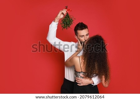 Happy couple kissing under mistletoe bunch on red background