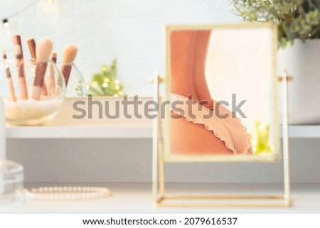 Reflection in table mirror of woman in underwear on dressing table with make up accessories. Self-Care. 