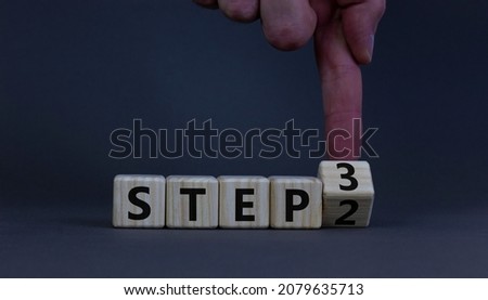 Step 2 or 3 symbol. Businessman turns a wooden cube and changes words Step 2 to Step 3. Beautiful grey table, grey background, copy space. Business and Step 2 or 3 planning concept. Royalty-Free Stock Photo #2079635713
