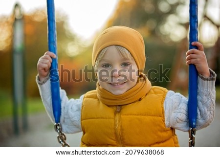 Happy child, playing with in autumn park on a sunny day, foliage and leaves all around him, swinging