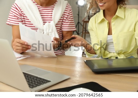 Professional retoucher with colleague working at desk in photo studio, closeup