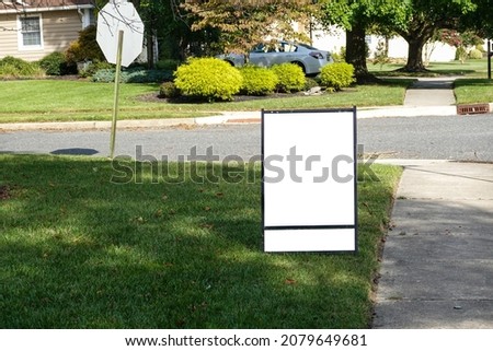 Blank white lawn sign with two panels on a green grass lawn near a sidewalk and street on a sunny day