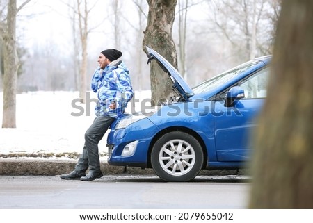 Stressed young man talking by phone near broken car outdoors