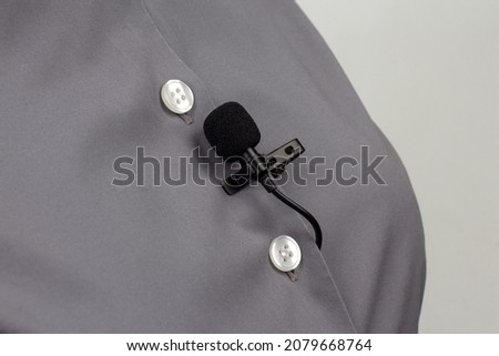 The lavalier microphone is secured with a clip on a gray women's shirt close-up. Audio recording of the sound of the voice on a condenser microphone.