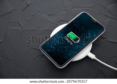 Mobile smart phone on wireless charging device on dark background. Icon battery and charging progress lighting on screen.smartphones connected to power source.low battery level problems.Plugged Phone.