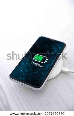 Mobile smart phone on wireless charging device on white background. Icon battery and charging progress lighting on screen.smartphones connected to power source.low battery level problems.Plugged