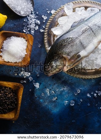 Fresh fish on ice cubes, in wooden bowls - salt and pepper. Preparation of fish and seafood dishes. Salting, marinating fish. Restaurant, hotel, home cooking, culinary blog. High angle view.