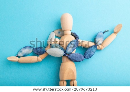 Wooden mannequin with blue agate beads on blue pastel background. copy space, isolated, luxury, bad taste, raunch, concept.