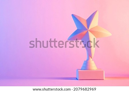 Small 3D star trophy award statuette with shadow, standing against purple and pink gradient color background with copy space