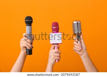 Female hands with modern microphones on color background
