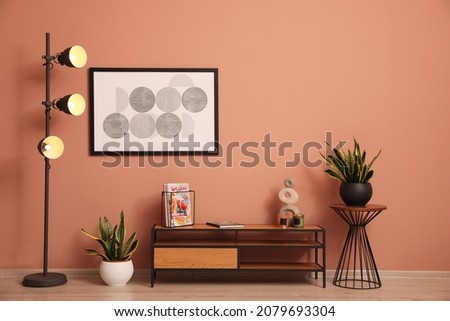 Stylish room interior with wooden cabinet, lamp and beautiful houseplants near pale pink wall