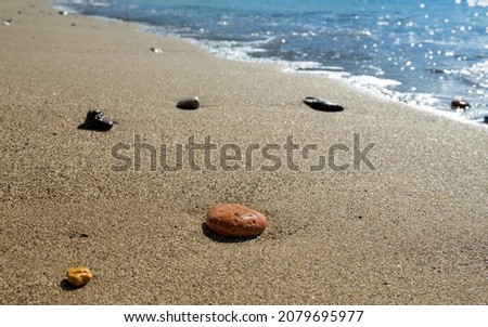 Colorful pebbles on the sand by the seashore. The orange colored stone in the foreground is in selective focus. The sea and sands are out of focus.