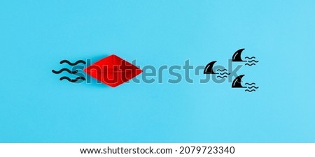 Danger, risk, threat or insurance concept. Red paper boat moves towards a group of sharks on blue background. Royalty-Free Stock Photo #2079723340