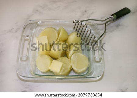 Boiled potatoes with butter and kosher salt on a small baking dish and a bean smasher on the side. Making mashed potatoes. Royalty-Free Stock Photo #2079730654