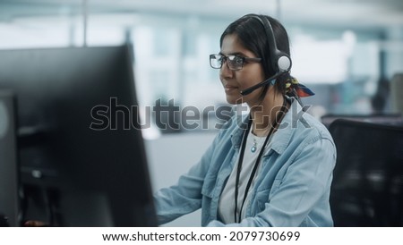 Call Center Office: Portrait of Friendy Indian Female IT Customer Support Specialist Working on Computer. Business Entrepreneur Using Headset to Talk with Client via Online Video Conference Call Royalty-Free Stock Photo #2079730699