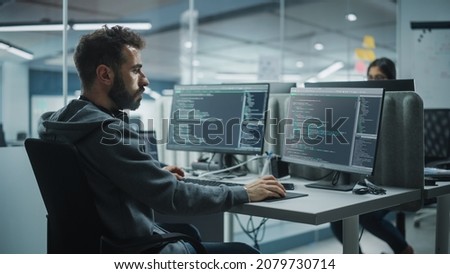 Diverse Office: IT Programmer Working on Desktop Computer. Male Specialist Creating Innovative Software Engineer Developing App, Program, Video Game. Terminal with Coding Language. Over Shoulder Royalty-Free Stock Photo #2079730714