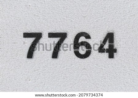 Black Number 7764 on the white wall. Spray paint. Number seven thousand seven hundred and sixty four.