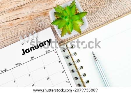 The January 2022 desk calendar and open diary with pen on wooden background.