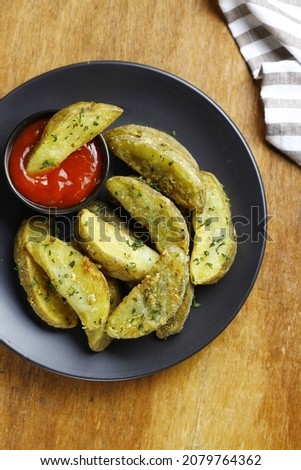 potato wedges served on black plate with tomato sauce. top view picture and wooden background 
