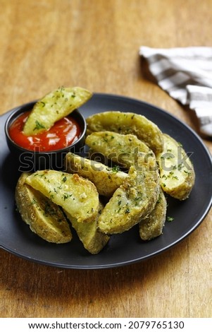 potato wedges served on black plate with tomato sauce. close up picture and wooden background 