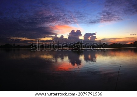 Stunning views of a beautiful sunset or sunrise over a pond or lake in spring or early summer in the evening. With a cloudy sky and grass and flowers in front of the landscape. Reflecting water.