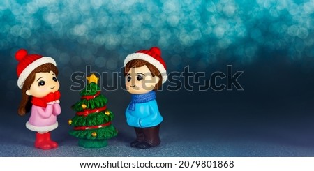 Festive horizontal banner. New Year's idea. Figurines of children at the Christmas tree on a blue background. Copy Space