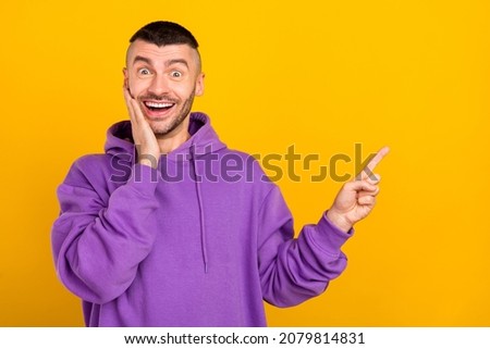Photo of cool young brunet guy point empty space wear purple hoodie isolated on yellow color background