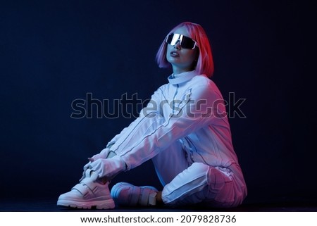 Woman in futuristic costume. Female in modern VR glasses interacting with network while having virtual reality experience. Augmented reality game, future technology, AI concept. VR. Neon blue light. Royalty-Free Stock Photo #2079828736
