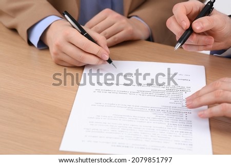 Businesspeople signing contract at wooden table, closeup of hands